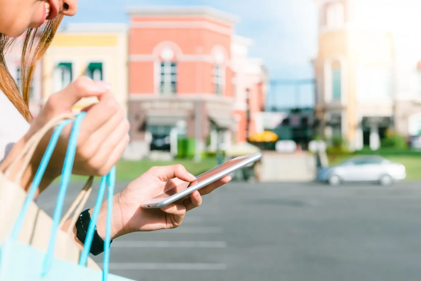 Close-up of a young woman carrying shopping bags in her hand and chatting on her phone after shopping.