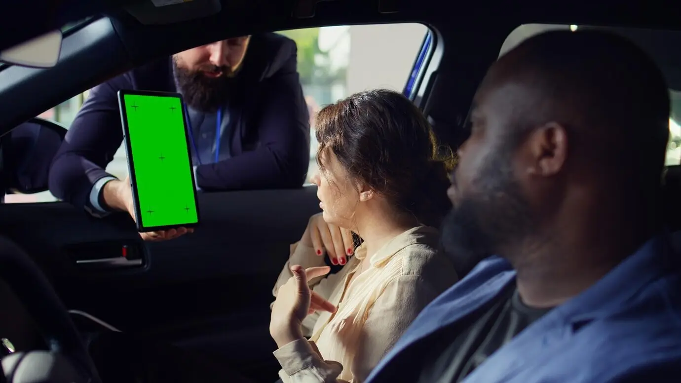 A sales representative presents vehicle add-on options to clients on a tablet with a green screen.
