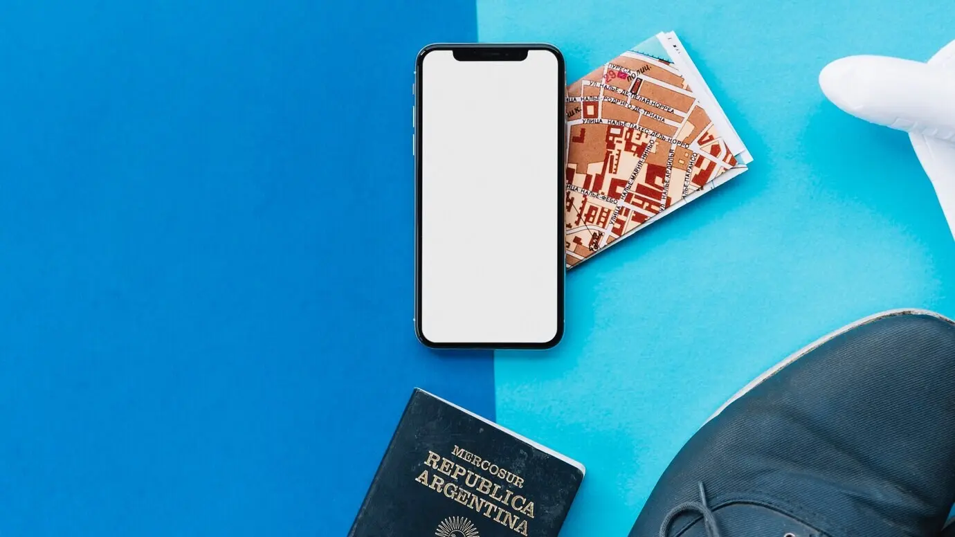 Smartphone displaying a white screen; map; passport; toy airplane; and shoes on a light and dark background.