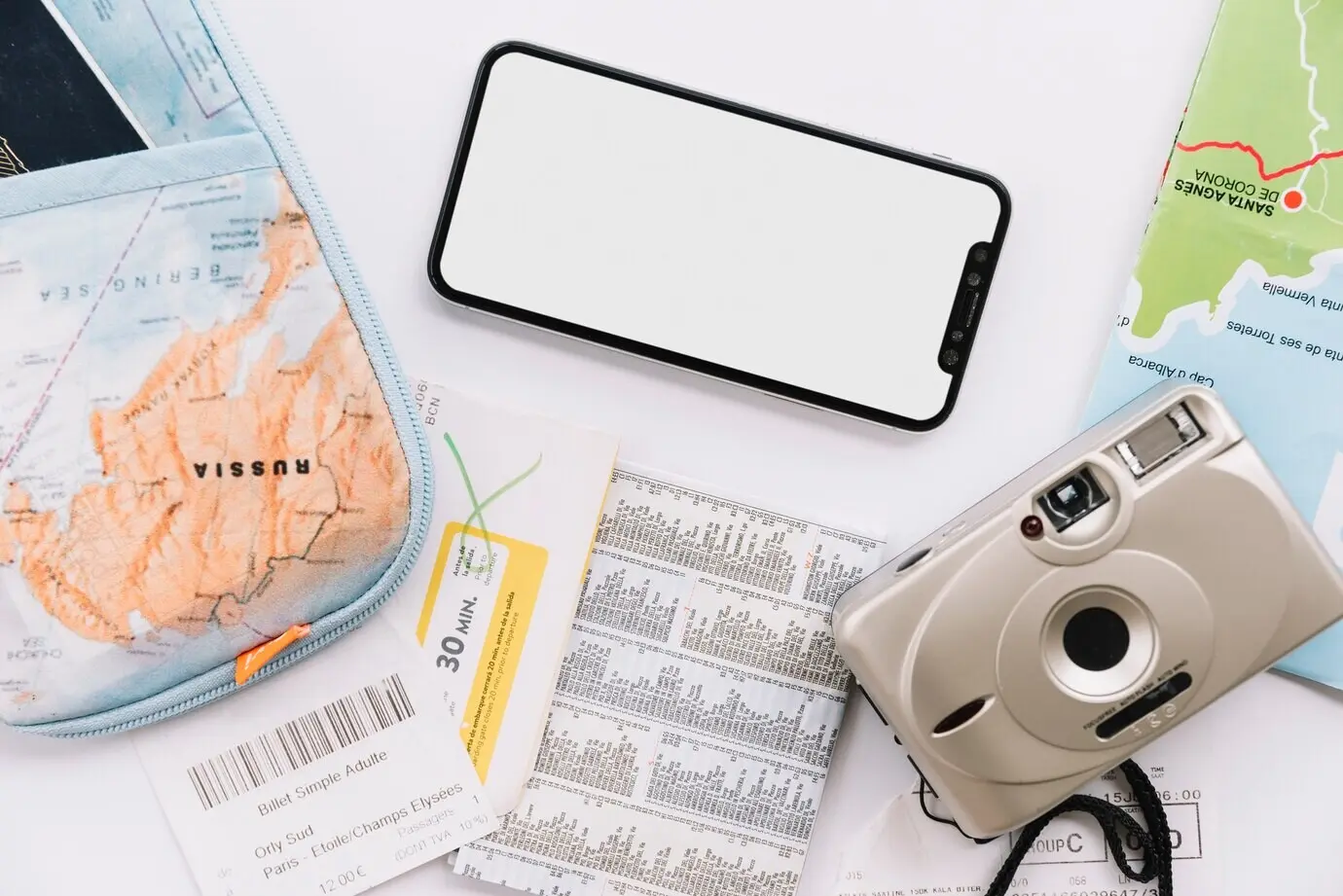 A pouch, a map, a digital camera, and a cell phone with a blank screen on a white background.